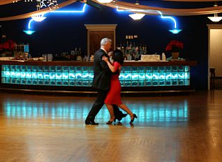 Woman in red dress dancing the Rumba with man in black suit by bar