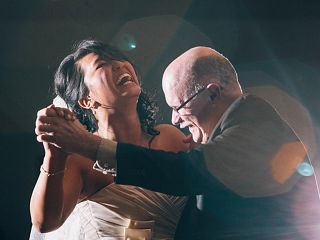 Woman in wedding gown laughing while dancing with man in suit